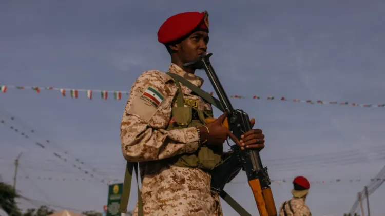 جندي من صومالي لاند يرتدي زيًا عسكريًا ويحمل سلاحًا، مع خلفية تظهر الأعلام الملونة، تعبيرًا عن الاستعدادات للاحتفال بالاستقلال.