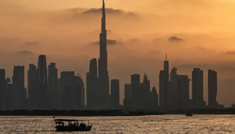 غروب الشمس خلف برج خليفة في دبي، مع قارب صغير يبحر في المياه، يعكس التحديات التي تواجه قطاع الشحن في ظل الأزمات الحالية.