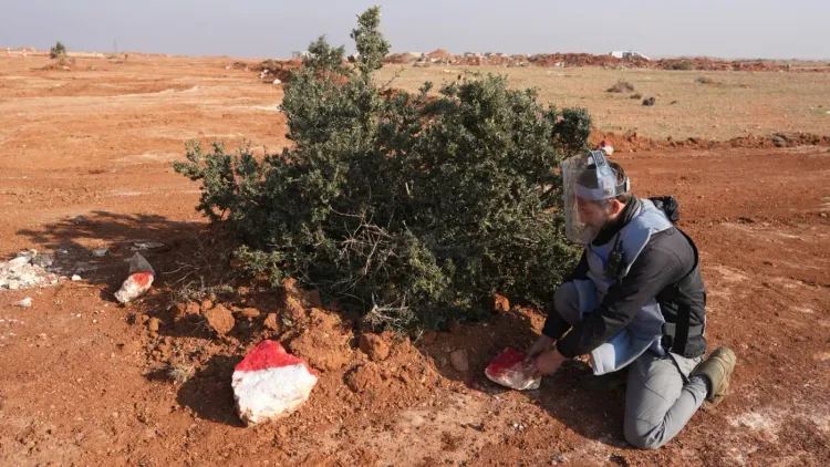 عامل إزالة ألغام يرتدي خوذة واقية، يعمل على تحديد موقع لغم مدفون في منطقة زراعية شمال غرب سوريا، مما يعكس خطر الألغام المتبقية.