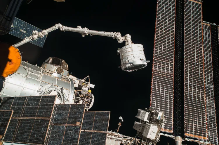 الذراع الآلي الكندي Canadarm2 معلق على محطة الفضاء الدولية، يبرز تعطل الذراع الذي يؤثر على عمليات الشحن والصيانة في المحطة.