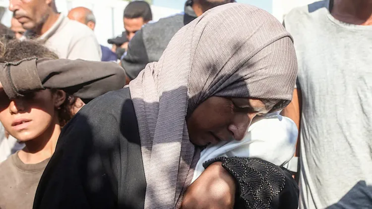 امرأة فلسطينية ترتدي الحجاب تعبر عن حزن عميق وسط حشد من الناس في قطاع غزة، تعكس معاناة النساء الحوامل في ظل ارتفاع معدلات الإجهاض بسبب الحرب والأوضاع الإنسانية الصعبة.