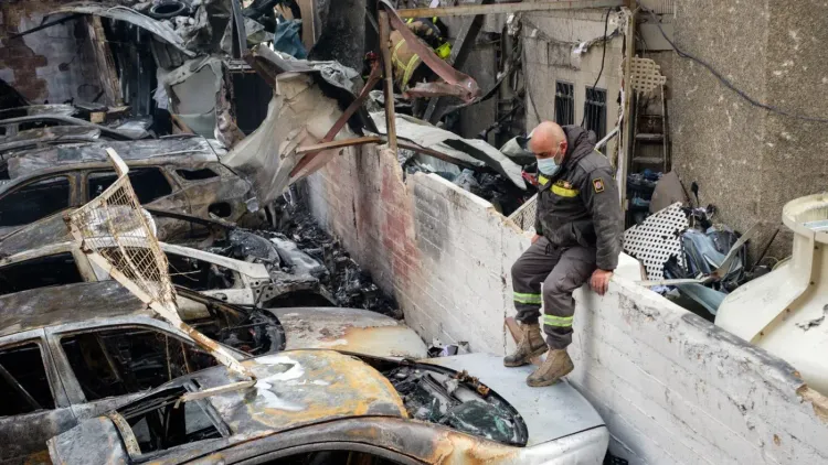 رجل إطفاء يجلس على حائط منخفض بجوار سيارات محترقة، في موقع دمار بعد غارة جوية في بيروت، مع آثار الدخان والحطام حوله.