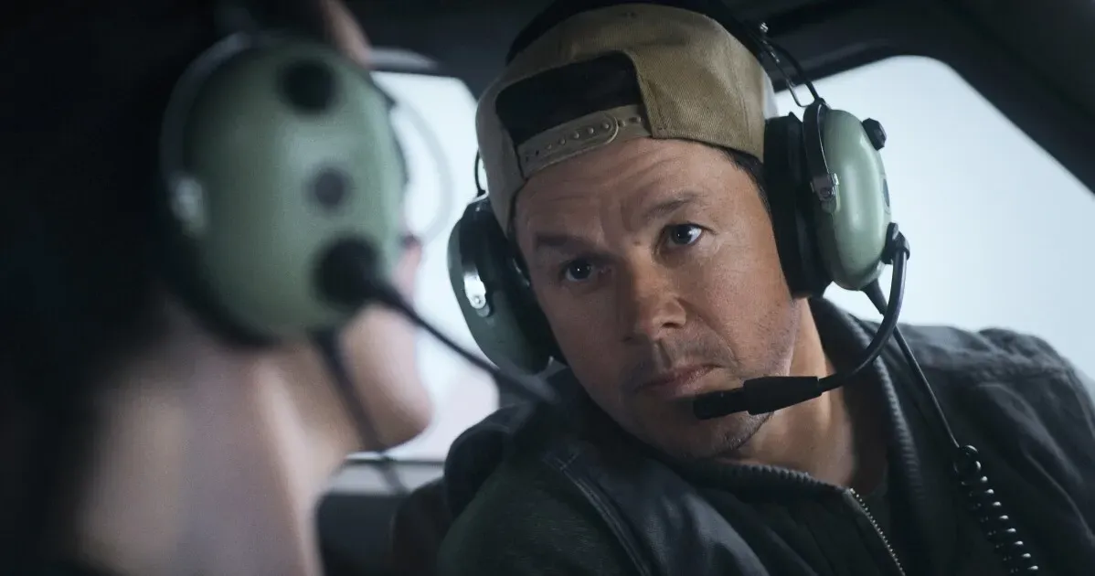 مشهد من فيلم "Flight Risk" يظهر الممثل مارك والبرغ مرتديًا سماعة طيران وهو يتحدث مع راكب في الطائرة.