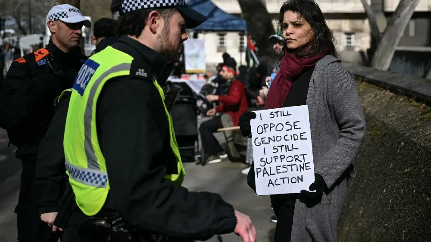 امرأة تحمل لافتة مكتوب عليها "ما زلت أعارض الإبادة الجماعية، ما زلت أدعم العمل الفلسطيني" أثناء احتجاج في لندن، مع وجود شرطة بالقرب منها.