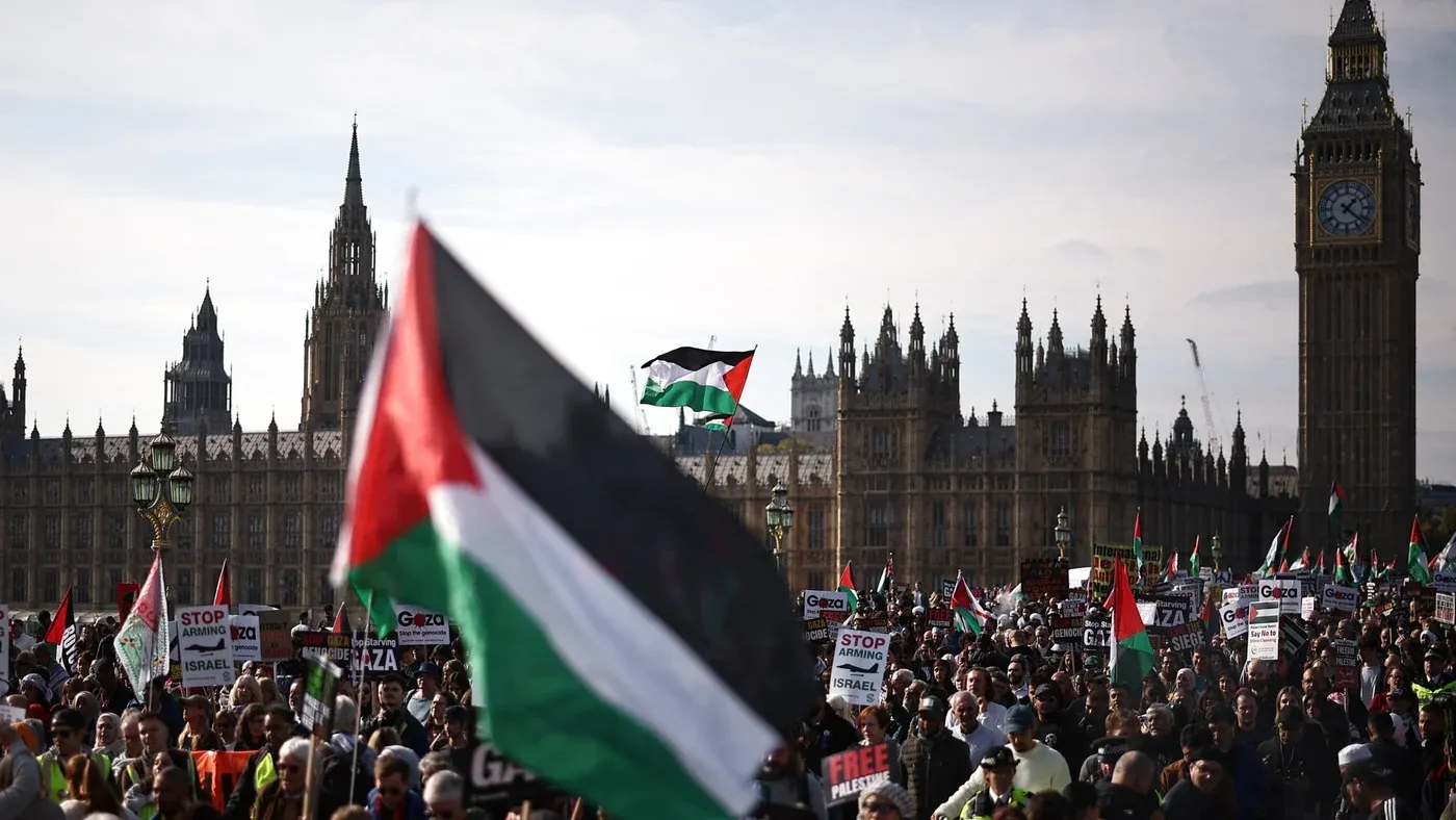 مظاهرة حاشدة في لندن لدعم فلسطين، حيث يرفع المحتجون الأعلام الفلسطينية واللافتات، مع معالم البرلمان البريطاني في الخلفية.