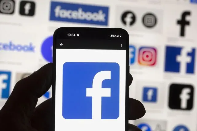 شخص يحمل هاتفًا ذكيًا يظهر شعار فيسبوك، مع خلفية تضم شعارات منصات التواصل الاجتماعي الأخرى مثل إنستغرام.