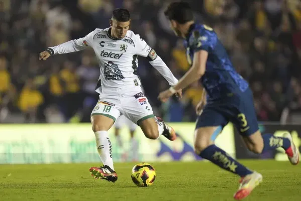 لاعب كرة قدم يرتدي زي نادي ليون المكسيكي يسدد الكرة خلال مباراة، مع وجود لاعب منافس في الخلفية، مما يعكس التنافس في كأس العالم للأندية.