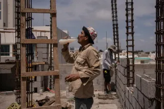 عامل بناء يشرب الماء أثناء العمل في موقع إنشاء، مع تسليط الضوء على تأثير الإجهاد الحراري في البيئات الحارة.