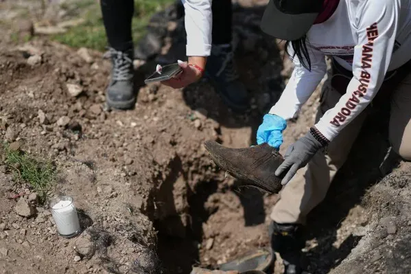 تظهر الصورة أفرادًا من مجموعة بحثية يقومون بالتحقق من موقع دفن محتمل، حيث يحمل أحدهم حذاءً في منطقة حفر.