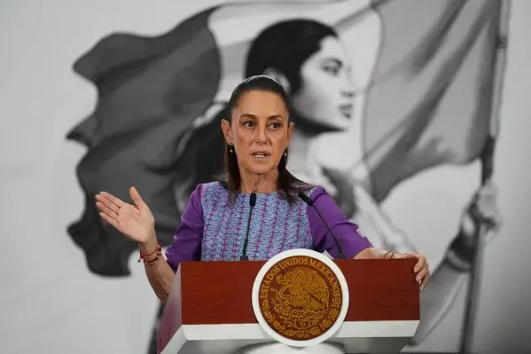 الرئيسة المكسيكية كلوديا شينباوم تتحدث خلال مؤتمر صحفي، مع خلفية تظهر امرأة تحمل علم المكسيك، تعبيرًا عن السيادة الوطنية.