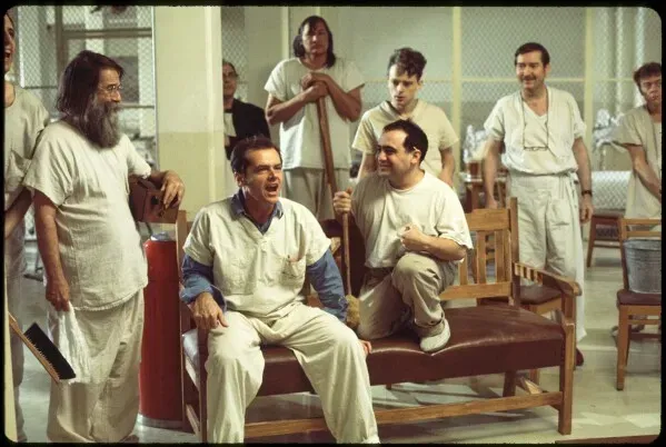 مشهد من فيلم "One Flew Over the Cuckoo's Nest" يظهر جاك نيكلسون مع مجموعة من الممثلين في مستشفى نفسي، يعكس أجواء العمل والتعاون بينهم.