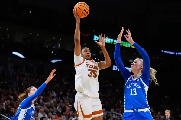 لاعبة كرة سلة من فريق تكساس تسجل نقطة خلال مباراة ضد كنتاكي، مع لاعبتين من الفريق المنافس تحاولان الدفاع عنها.