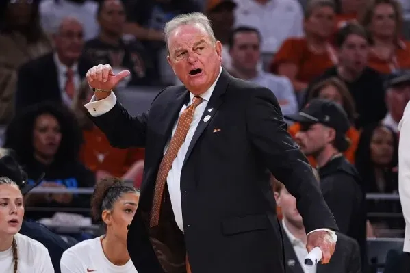 مدرب فريق تكساس في كرة السلة النسائية، فيك شيفر، أثناء توجيه تعليماته خلال مباراة في بطولة NCAA، مع خلفية من الجمهور.