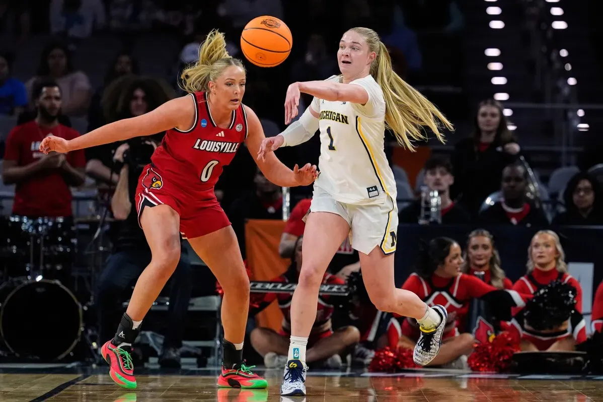 تظهر لاعبتان من فريق ميشيغان وفريق لويزفيل في لحظة تنافسية خلال مباراة كرة السلة، حيث تسعى كل منهما للاستحواذ على الكرة.