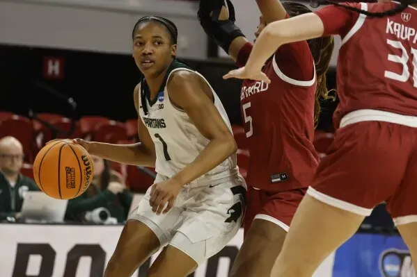 لاعبة كرة سلة من ولاية ميشيغان تتجاوز لاعبتين من فريق هارفارد، تحمل الكرة في مباراة NCAA.