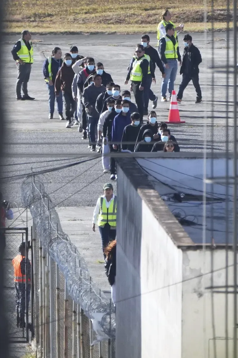 نازحون يسيرون تحت حراسة في مطار غواتيمالا بعد ترحيلهم، حيث يظهر عدد منهم يرتدون الكمامات ومكبلين بالحبال.