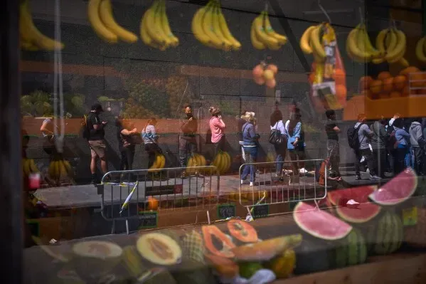 طابور من المهاجرين غير الموثقين ينتظرون في مدريد لتقديم طلبات الحصول على وضع قانوني، مع عرض لفاكهة في المقدمة.