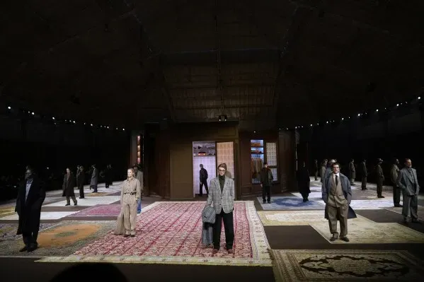عرض أزياء في ميلانو يظهر عارضين يرتدون ملابس أنيقة على منصة مزينة بسجاد ملون، مع التركيز على التصاميم العصرية والمبتكرة.
