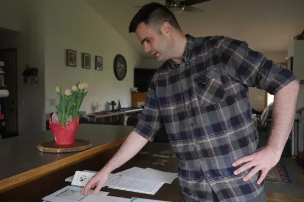 رجل يقف أمام طاولة، يستعرض مستندات تتعلق بطلب الجنسية الكندية، مع زهور في وعاء بجانبه، تعبيرًا عن اهتمامه بالجنسية المزدوجة.