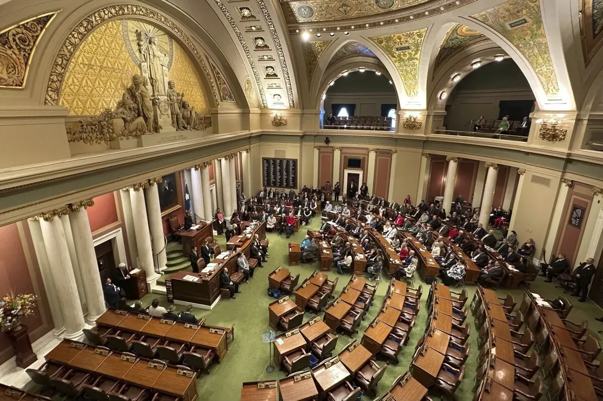 قاعة مجلس النواب في Minnesota، حيث يعقد المشرعون جلسة حوار مع وجود عدد كبير من الحضور، وسط تفاصيل معمارية مميزة وزخارف فاخرة.