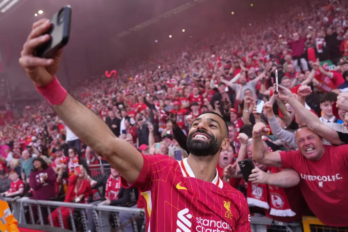 محمد صلاح يلتقط سيلفي مع جماهير ليفربول في ملعب أنفيلد، حيث يحتفل مع المشجعين بعد أداء مميز، وسط أجواء حماسية.