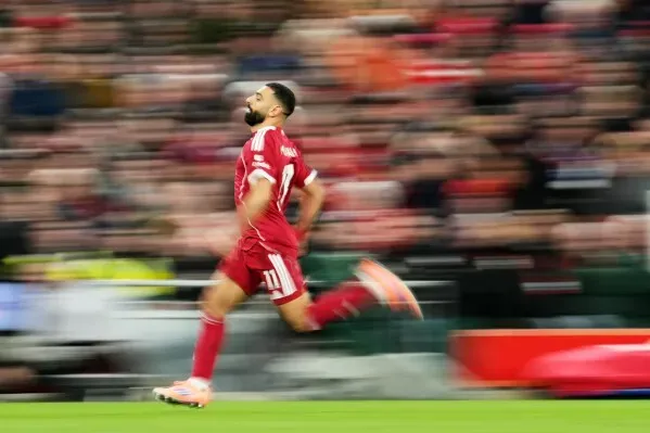 محمد صلاح، لاعب ليفربول، يركض في الملعب خلال مباراة، مع خلفية جماهيرية ضبابية تعكس حماس الجماهير.