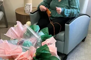 امرأة تجلس في كرسي، تحيك أخطبوطات ملونة من الغزل لتقديمها للأطفال في وحدة العناية المركزة لحديثي الولادة.