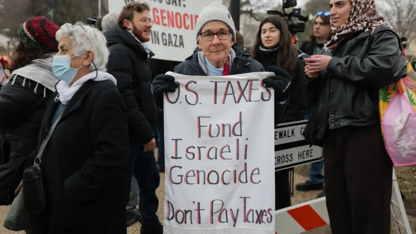امرأة مسنّة تحمل لافتة مكتوب عليها "ضرائب الولايات المتحدة تمول الإبادة الجماعية الإسرائيلية" في مظاهرة تعبر عن التعاطف مع الفلسطينيين.