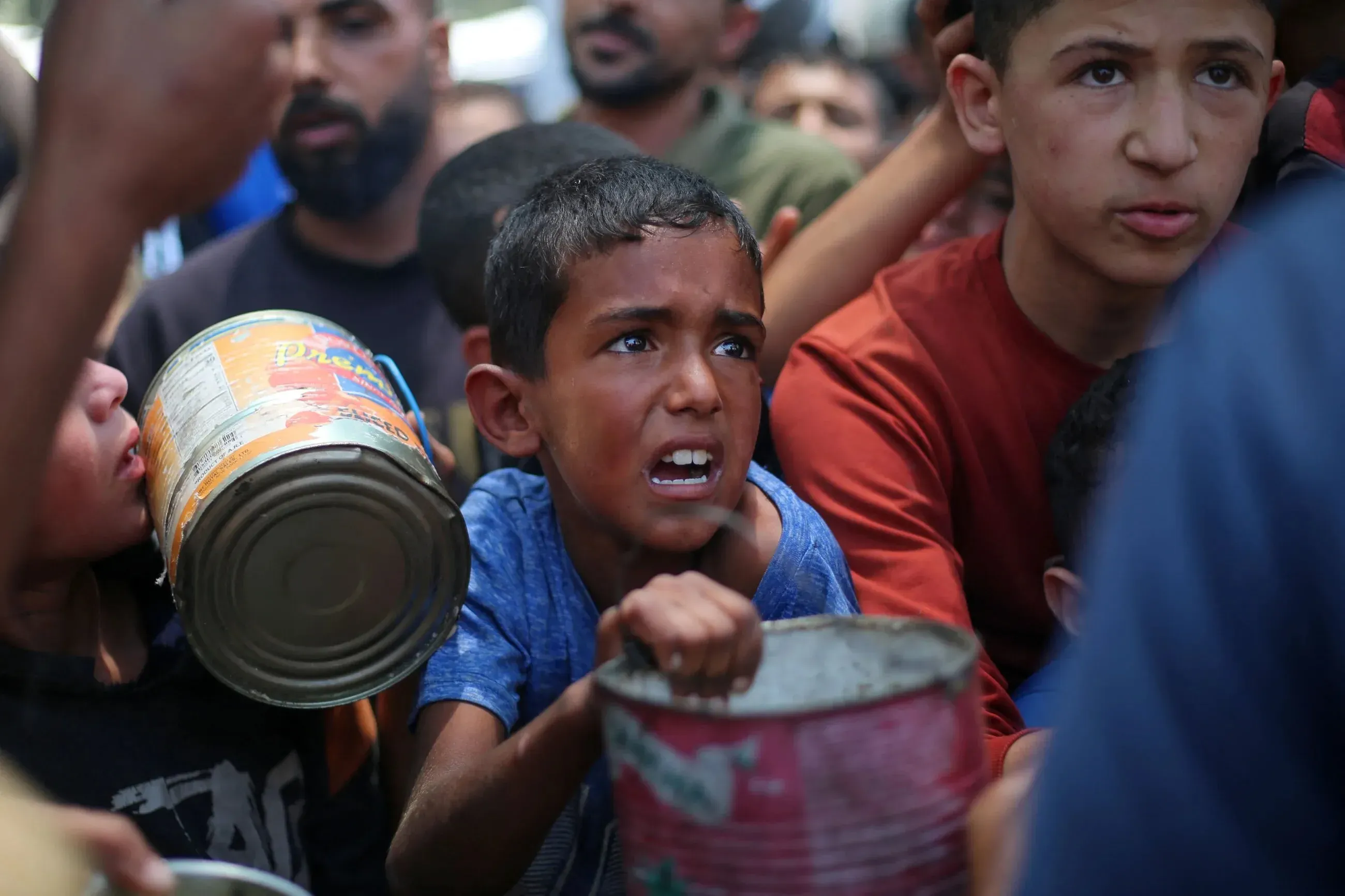 طفل فلسطيني يعبر عن معاناته أثناء انتظار المساعدات الغذائية في غزة، حيث يعاني السكان من نقص حاد في الإمدادات الأساسية.