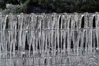 تتدلى أنياب الثلج المتجمد من سياج، مما يعكس تأثير العاصفة الجليدية التي اجتاحت الولايات المتحدة، مع درجات حرارة شديدة البرودة.