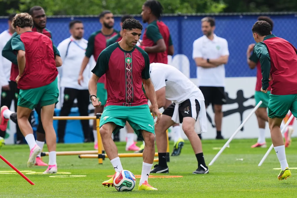 أشرف حكيمي، لاعب المنتخب المغربي، يتدرب مع زملائه في الفريق قبل مباراة كأس العالم، وسط أجواء تنافسية وحماسية.