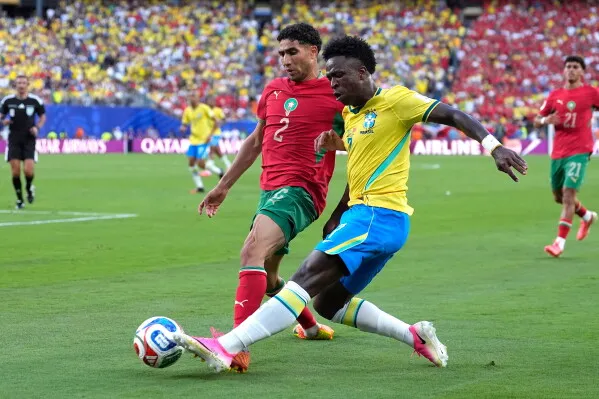 أشرف حكيمي، مدافع المنتخب المغربي، يتصدى لهجمة لاعب برازيلي خلال مباراة كأس العالم، وسط أجواء حماسية في الملعب.