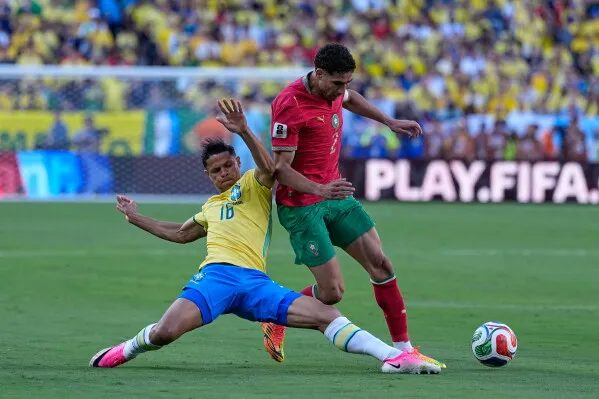 أشرف حكيمي، لاعب منتخب المغرب، يتصدى لهجمة خلال مباراة ضد البرازيل في كأس العالم، مع وجود جمهور خلفهم.