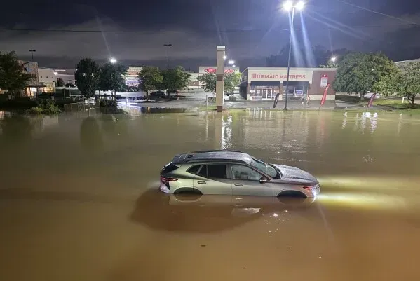 سيارة غارقة جزئيًا في مياه الفيضانات بعد هطول أمطار غزيرة في تينيسي، مع محلات تجارية مضاءة في الخلفية.