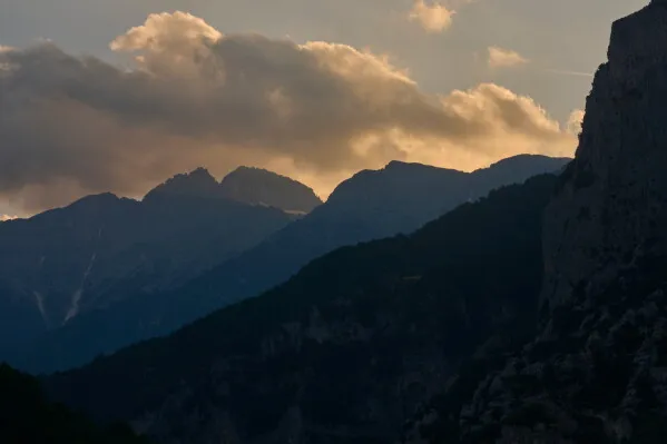 جبال أوليمبوس في اليونان تغطيها الغيوم عند الغروب، مع إبراز جمالها الطبيعي وتراثها الثقافي المرتبط بأساطير الإغريق القدماء.