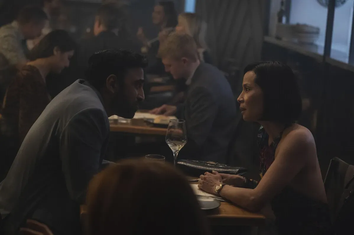 مشهد من مطعم حيث يتحدث رجل وامرأة بشكل حميمي، مع وجود زبائن آخرين في الخلفية، يعكس أجواء الفيلم "الرجل العجوز".