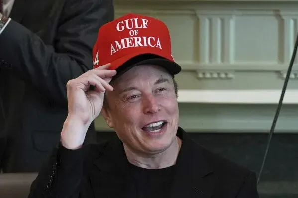إيلون ماسك يرتدي قبعة حمراء مكتوب عليها "GULF OF AMERICA" بينما يتحدث في غرفة روزفلت بالبيت الأبيض، معبرًا عن آرائه حول وزارة التعليم العالي.