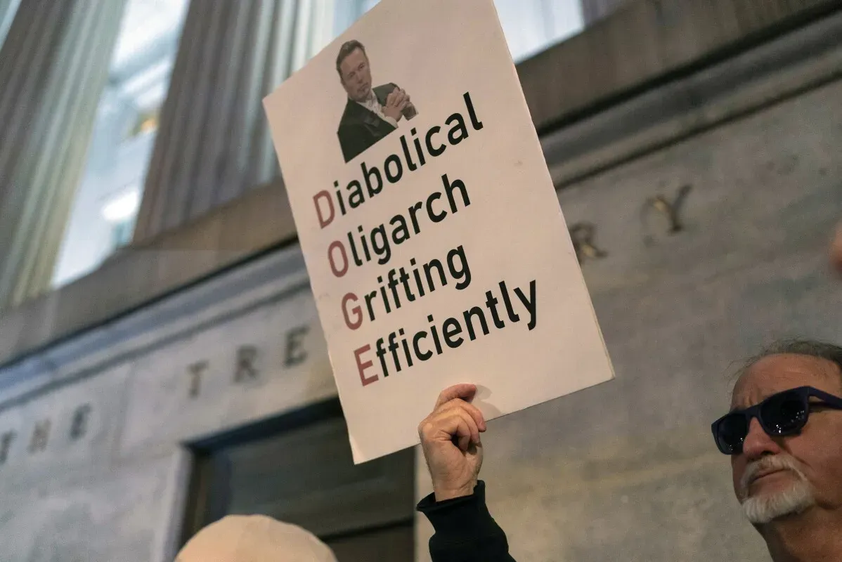 لافتة احتجاج تحمل عبارة "Diabolical Oligarch Grifting Efficiently" مع صورة إيلون ماسك، تعبر عن الانتقادات الموجهة له ولنفوذه في السياسة.