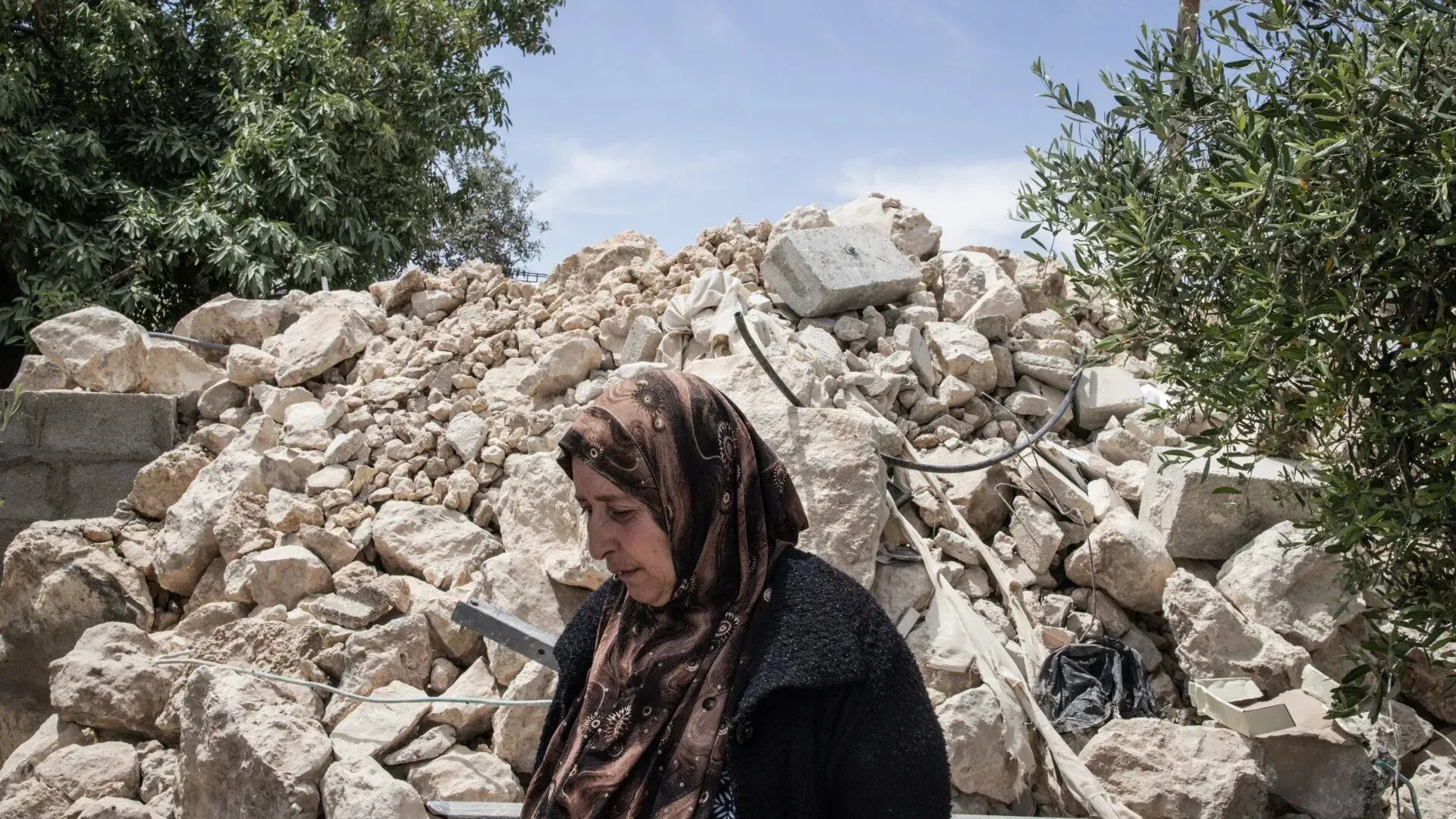امرأة فلسطينية واقفة أمام كومة من الأنقاض، تعكس آثار التدمير والاضطهاد في الأراضي المحتلة.