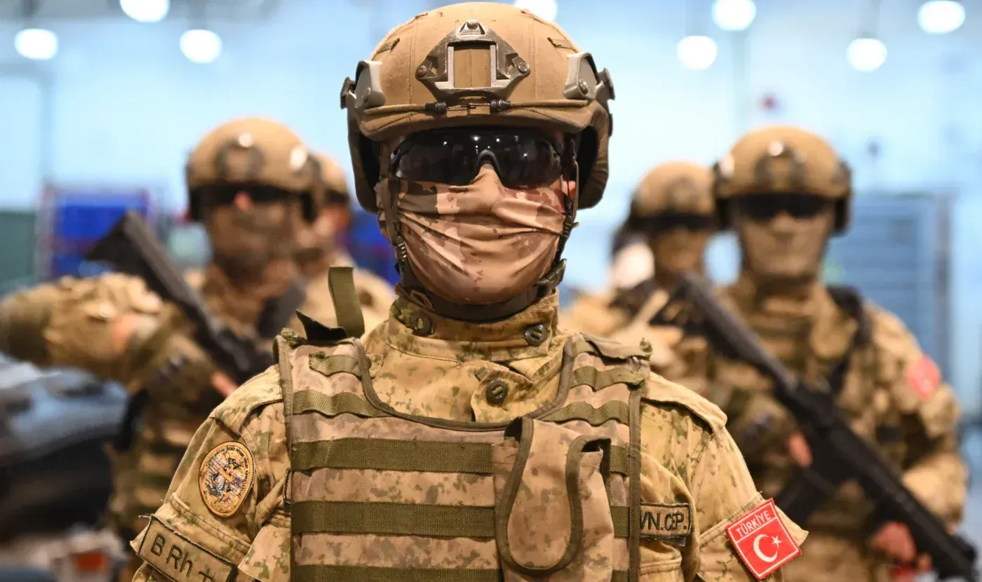 جنود أتراك يرتدون زيًا عسكريًا كاملًا، مع أسلحة ومعدات، في قاعدة عسكرية، مما يعكس استعداد تركيا لتعزيز قوة الناتو في المنطقة.