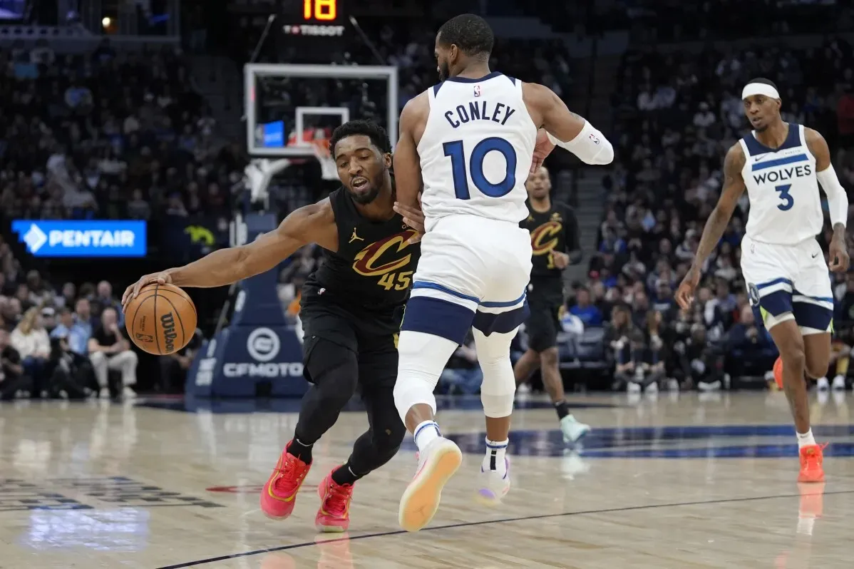 دونوفان ميتشل يحمل الكرة محاولًا تجاوز لاعب تمبروولفز، بينما يتنافس الفريقان في مباراة مثيرة NBA بملعب مينيسوتا.