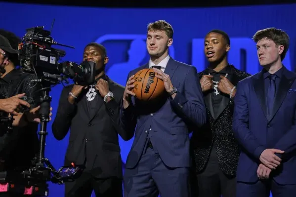 لاعبو كرة سلة يرتدون بدلات أنيقة خلال ليلة قرعة دوري الـNBA، مع أحدهم ممسكًا بكرة سلة، في أجواء احتفالية.