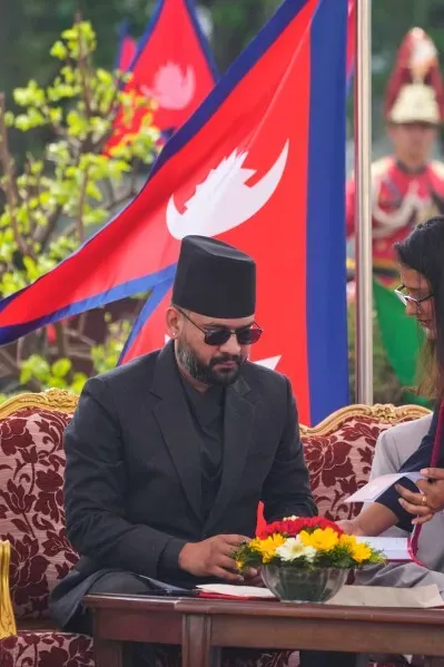 باليندرا شاه، أصغر رئيس وزراء نيبال، يجلس خلال مراسم أداء اليمين الدستورية، مع أعلام نيبالية خلفه وزهور أمامه.