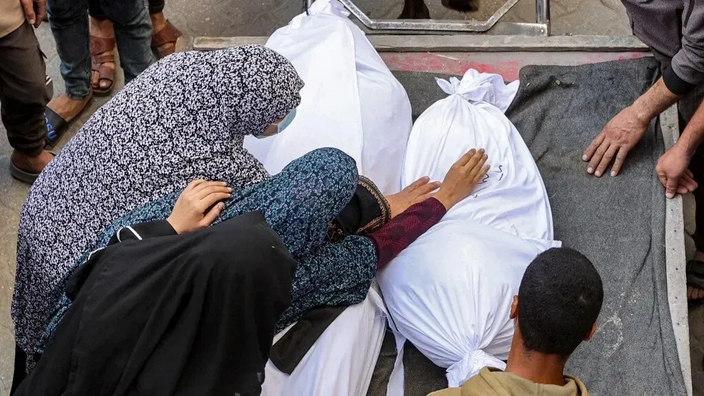 نساء وأطفال يشاركون في مراسم وداع، يلمسون أكياس الموتى المغلقة في غزة، وسط أجواء من الحزن الشديد نتيجة القصف الإسرائيلي.
