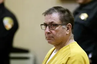 بول كانيرو، المدان بقتل أربعة من أقاربه، يظهر في قاعة المحكمة مرتديًا زي السجن الأصفر، مع وجود ضباط شرطة خلفه.