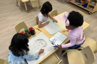 ثلاثة أطفال يعملون على رسوماتهم في فصل دراسي، مع التركيز على الإبداع والتعلم في بيئة رعاية الطفولة المبكرة في نيو مكسيكو.