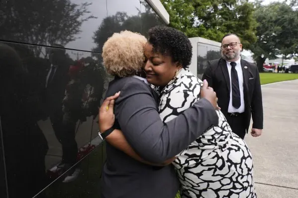 احتضان مؤثر بين امرأتين خلال مراسم إحياء ذكرى إعصار كاترينا في نيو أورليانز، مع وجود شخص ثالث في الخلفية.