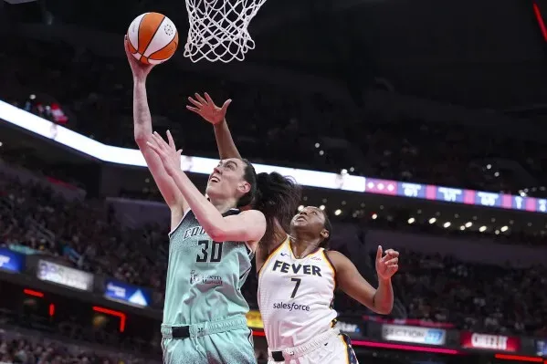 لاعبة كرة سلة تسجل نقطة تحت السلة بينما تحاول لاعبة أخرى منعها، في مباراة حماسية ضمن دوري WNBA.