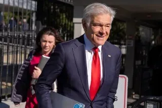 يظهر الدكتور محمد أوز مبتسمًا أثناء مغادرته مبنى حكومي، محاطًا بأشخاص آخرين، في سياق الجدل حول ادعاءاته بشأن الاحتيال في دور العجزة في لوس أنجلوس.