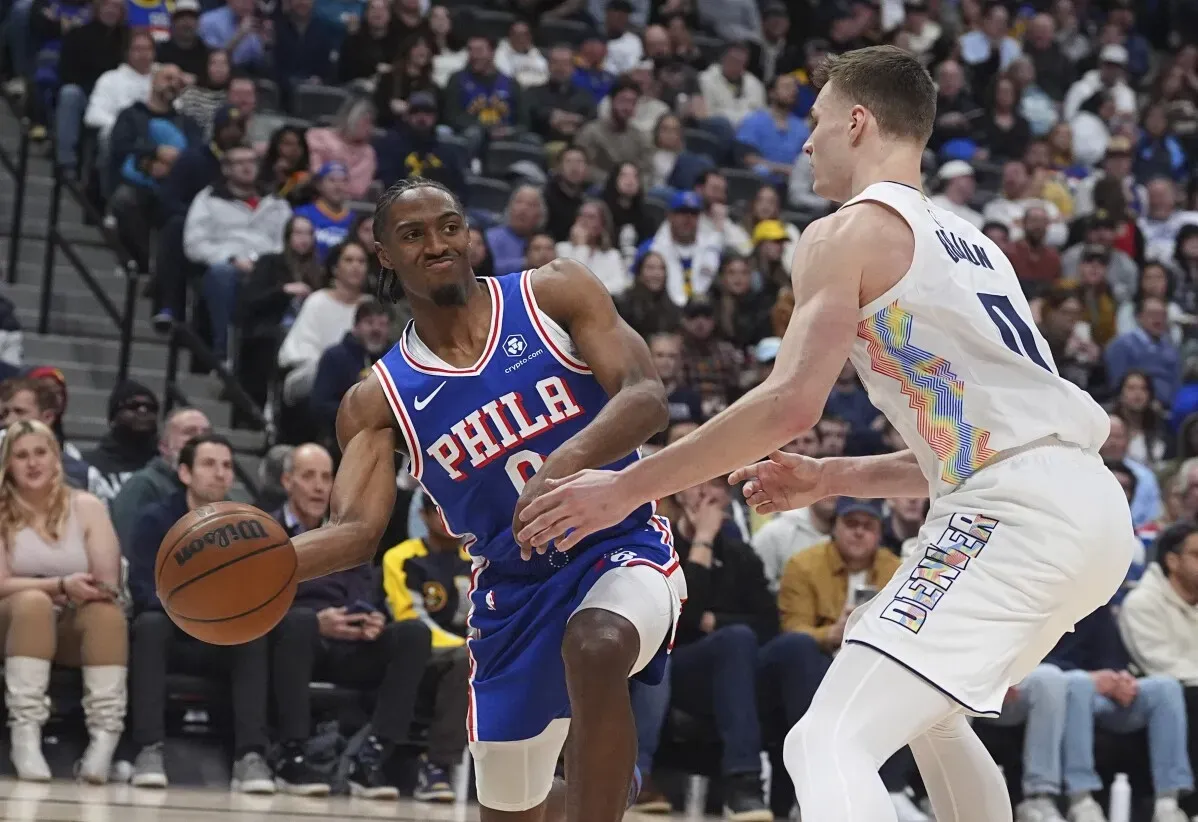 لاعب من فريق فيلادلفيا يستعرض مهارته في المراوغة في مواجهة لاعب من دنفر خلال مباراة NBA، مع حشد من المشجعين خلفهم.